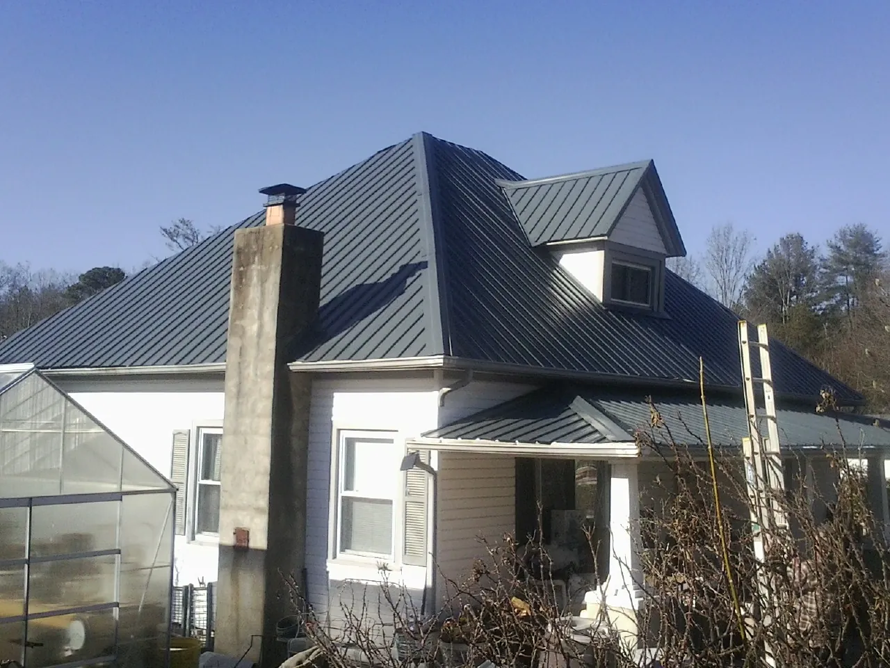 Dark blue standing seam metal roof on a white farmhouse with dormer — Slate & Tile Roof Repair by Roofing Brothers in Joplin