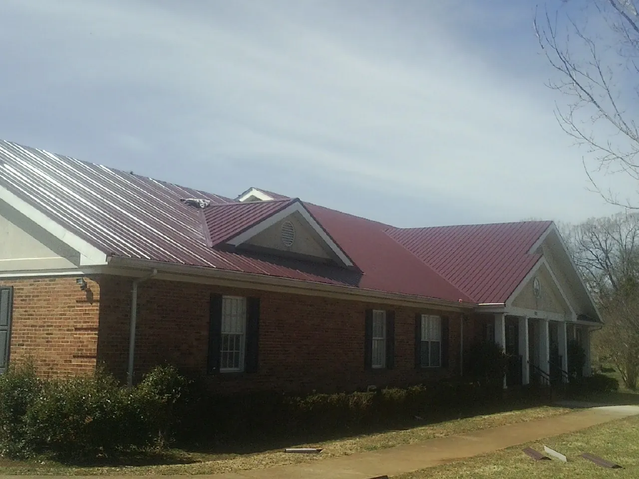 Red metal roof with gabled entries on a long brick building, from a Hail Damage Roof Repair job in Joplin