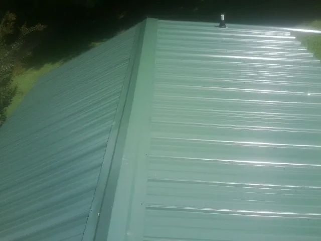 New green metal panels meeting at the ridge of a roof — Flat Roof Repair work by our crew in Joplin