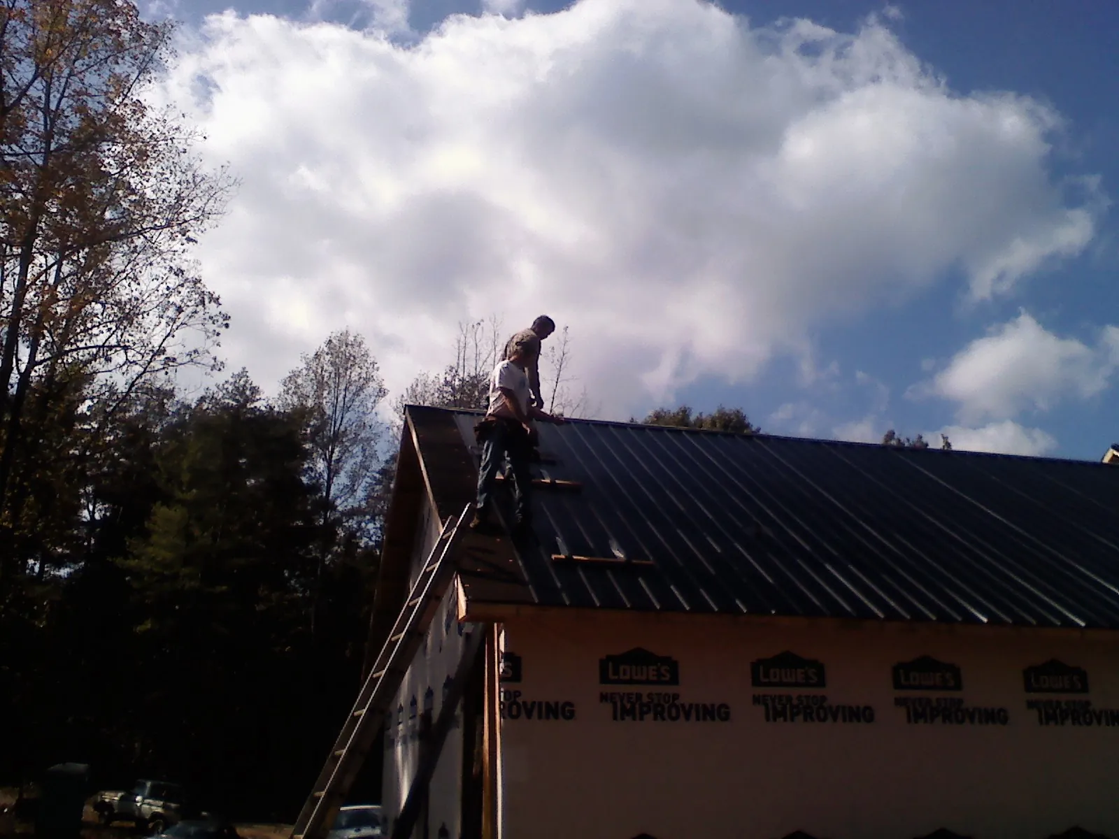 Roofer fastening dark metal panels high against a cloudy sky, from a Roof Inspection job in Joplin