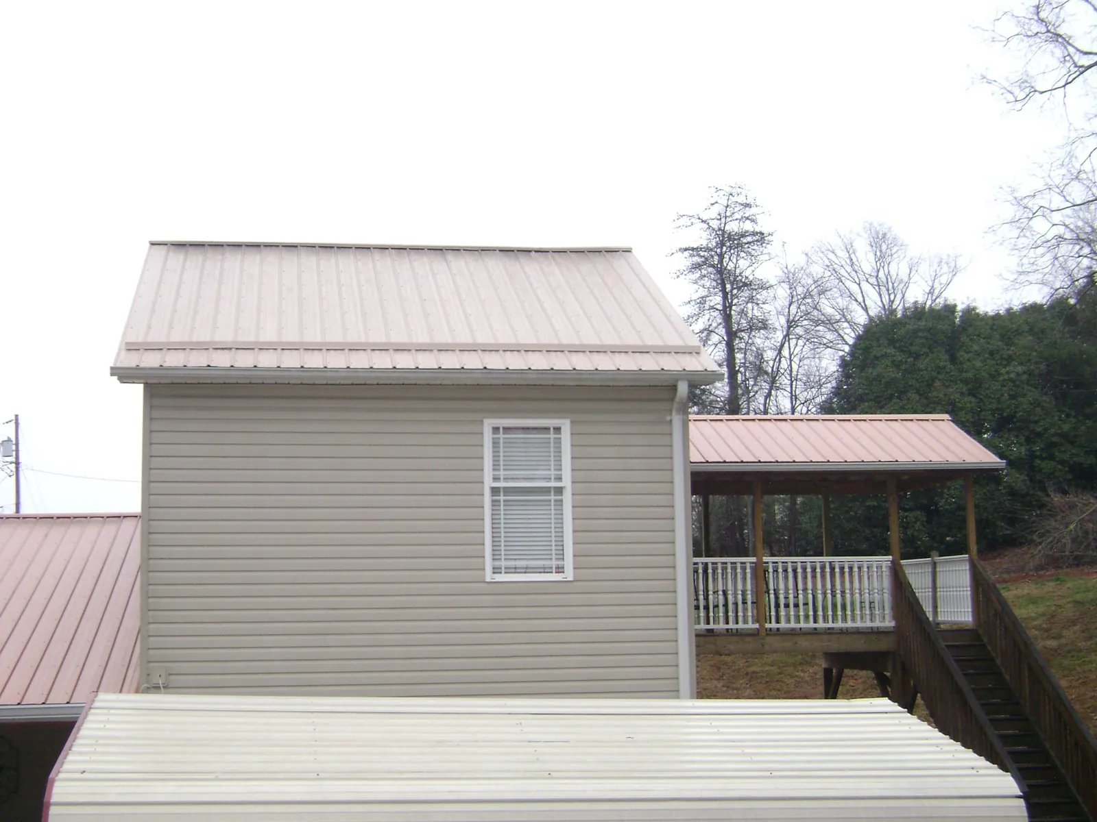 Tan metal roofs on a two story addition and attached porch, from a Roof Replacement job in Joplin