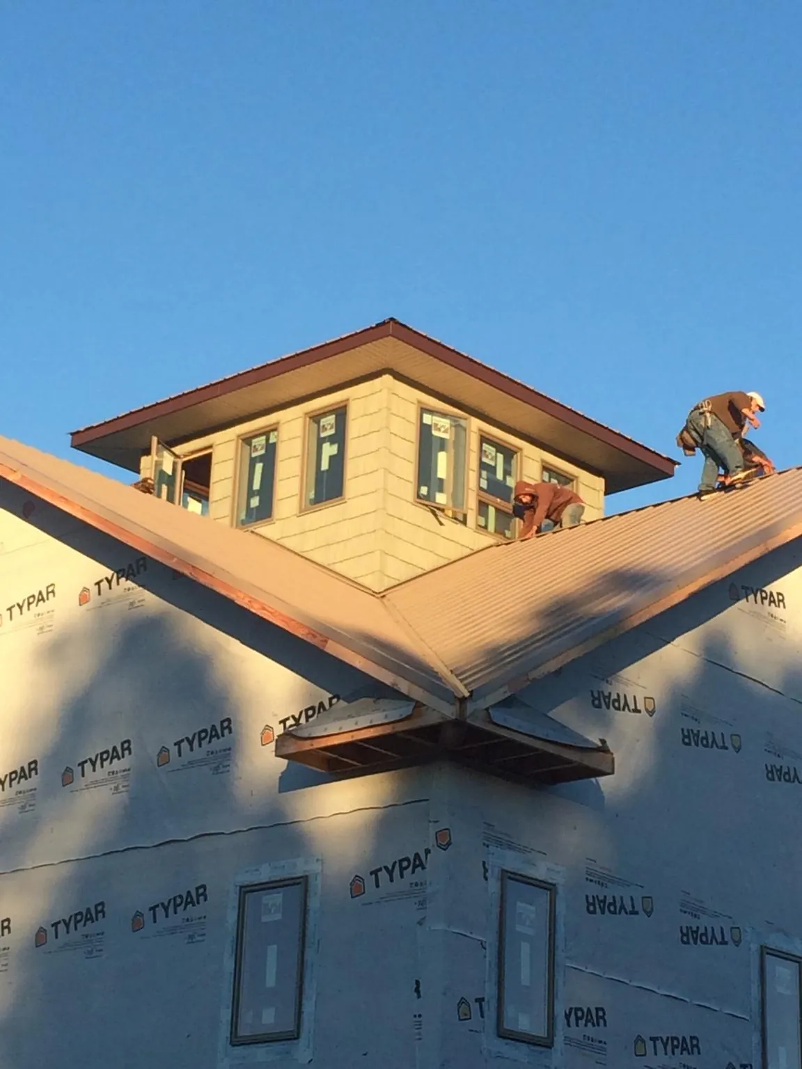 Roofers working around a rooftop cupola on a new metal roof at sunset — Roof Waterproofing in Joplin by Roofing Brothers